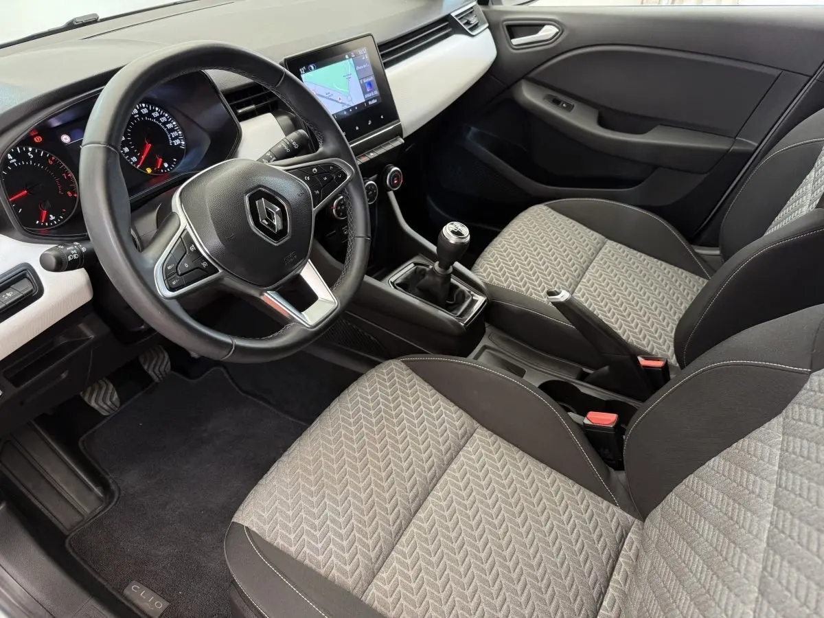 Vue intérieure côté conducteur de la Renault Clio 2023 avec volant cuir, écran tactile central et sièges gris à motifs.