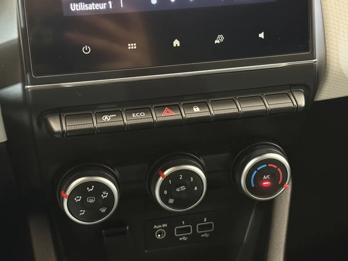 Gros plan sur la console centrale de la Renault Clio blanche 2023, montrant les commandes de climatisation et boutons fonctionnels.