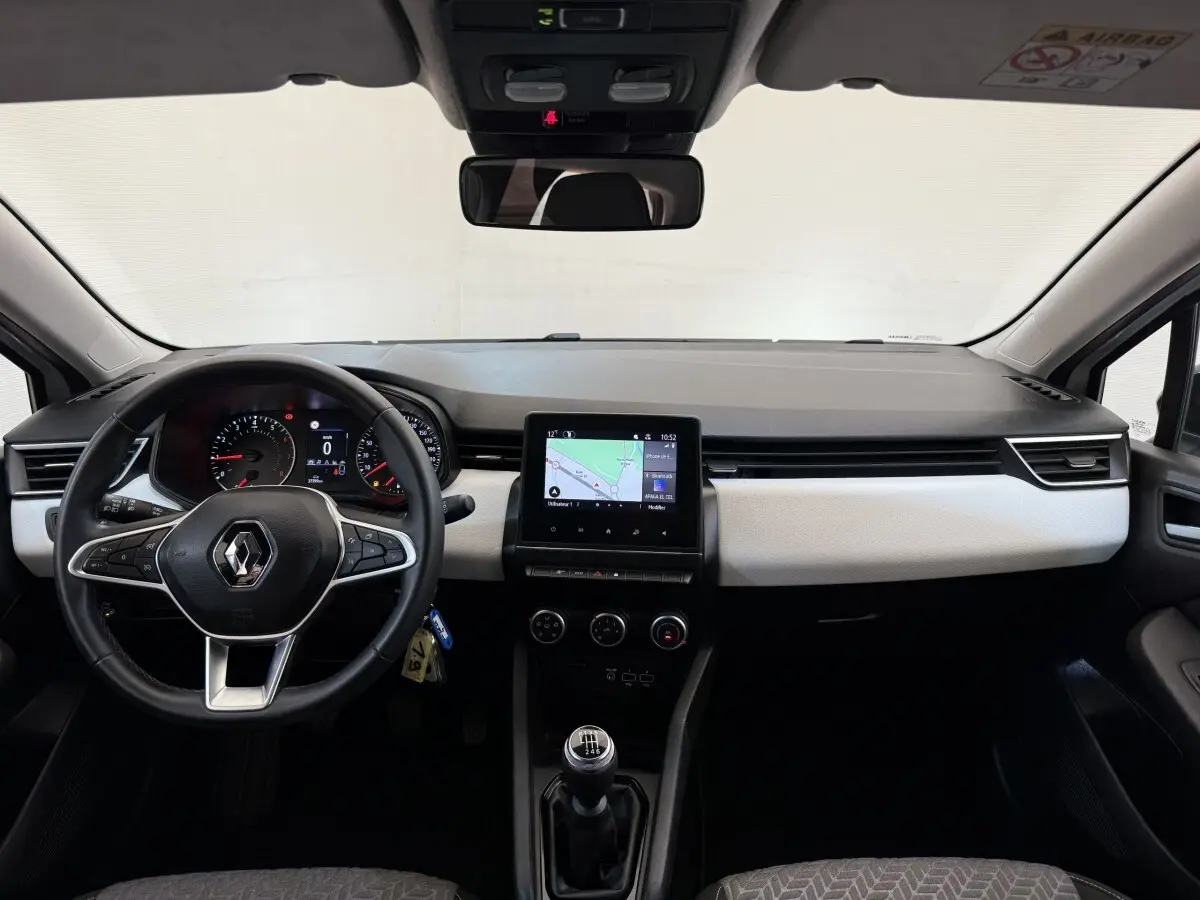 Vue intérieure frontale du tableau de bord de la Renault Clio blanche 2023 avec écran tactile central et volant cuir multifonctions.