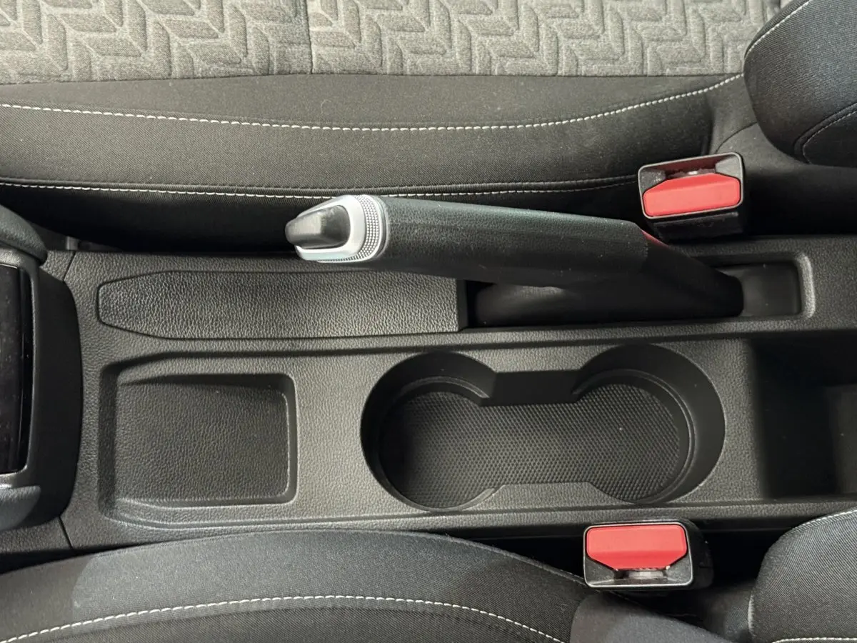 Vue rapprochée de la console centrale noire avec frein à main et porte-gobelets de la Renault Clio blanche Evolution TCe 100 GPL 2023.