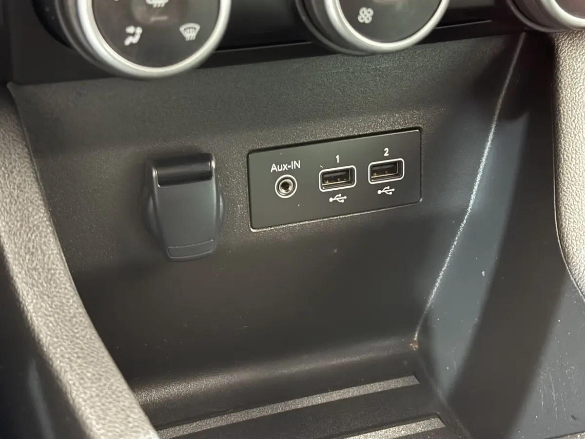 Gros plan sur la console centrale noire de la Renault Clio blanche Evolution TCe 100 GPL, montrant les ports USB et Aux-IN.