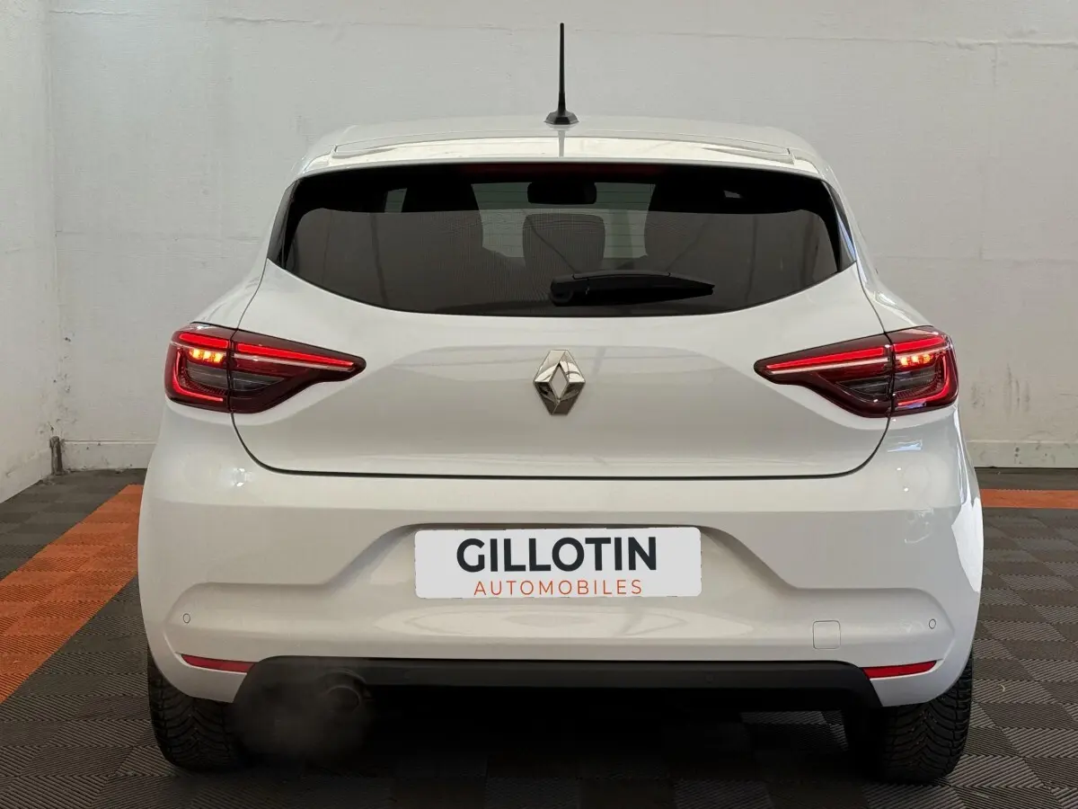 Vue arrière d'une Renault Clio blanche Evolution TCe 100 GPL avec feux arrière allumés dans un garage.