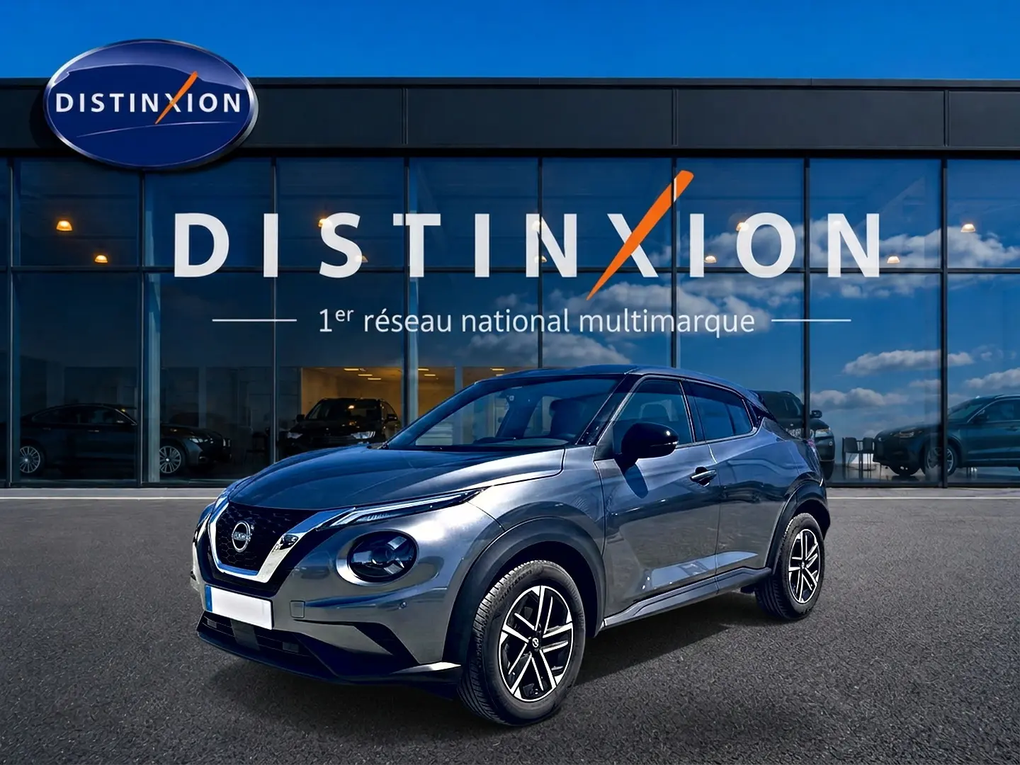 Nissan Juke gris 3/4 avant droit avec jantes alu, garé devant une vitrine Distinxion.