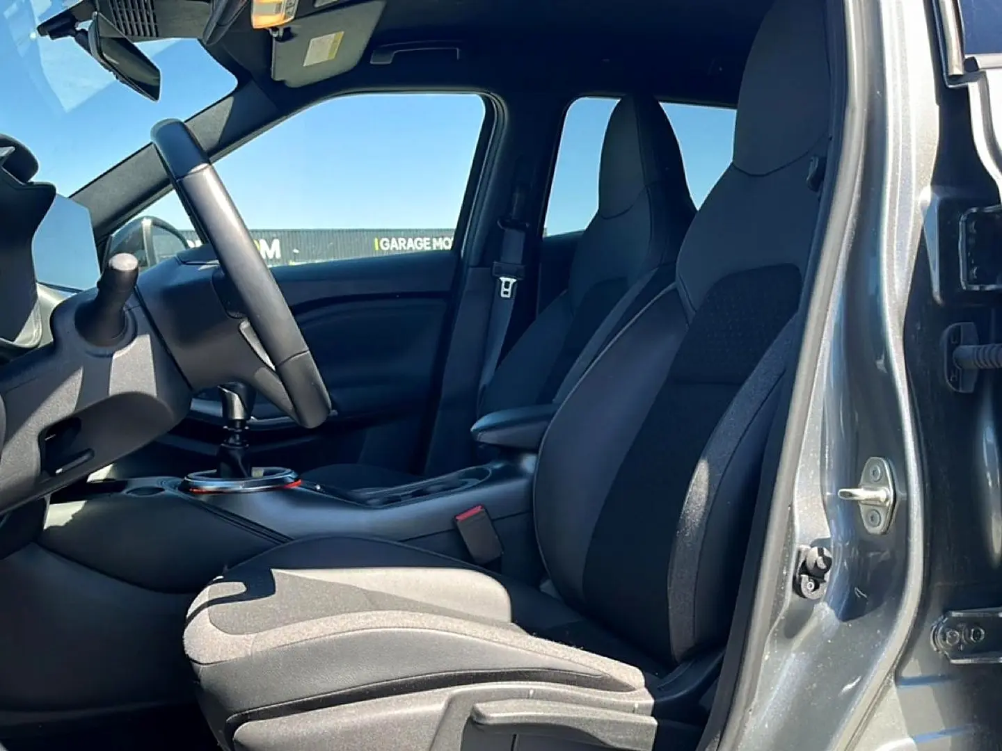 Vue intérieure côté conducteur du Nissan Juke gris 2025, avec sièges mixtes noir et gris et volant cuir multifonction.