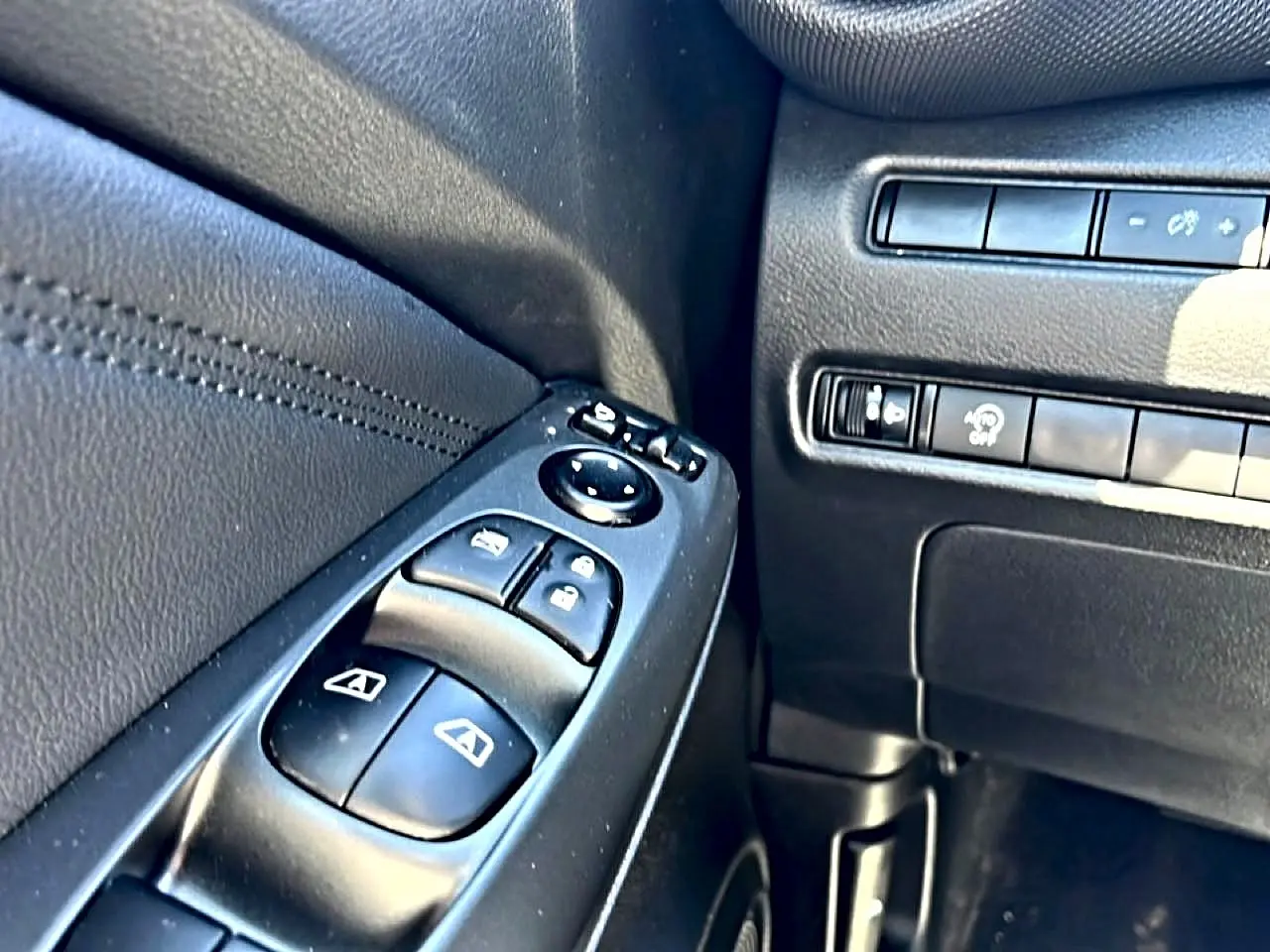 Gros plan sur les commandes de vitres électriques et rétroviseurs côté conducteur du Nissan Juke gris 2025.