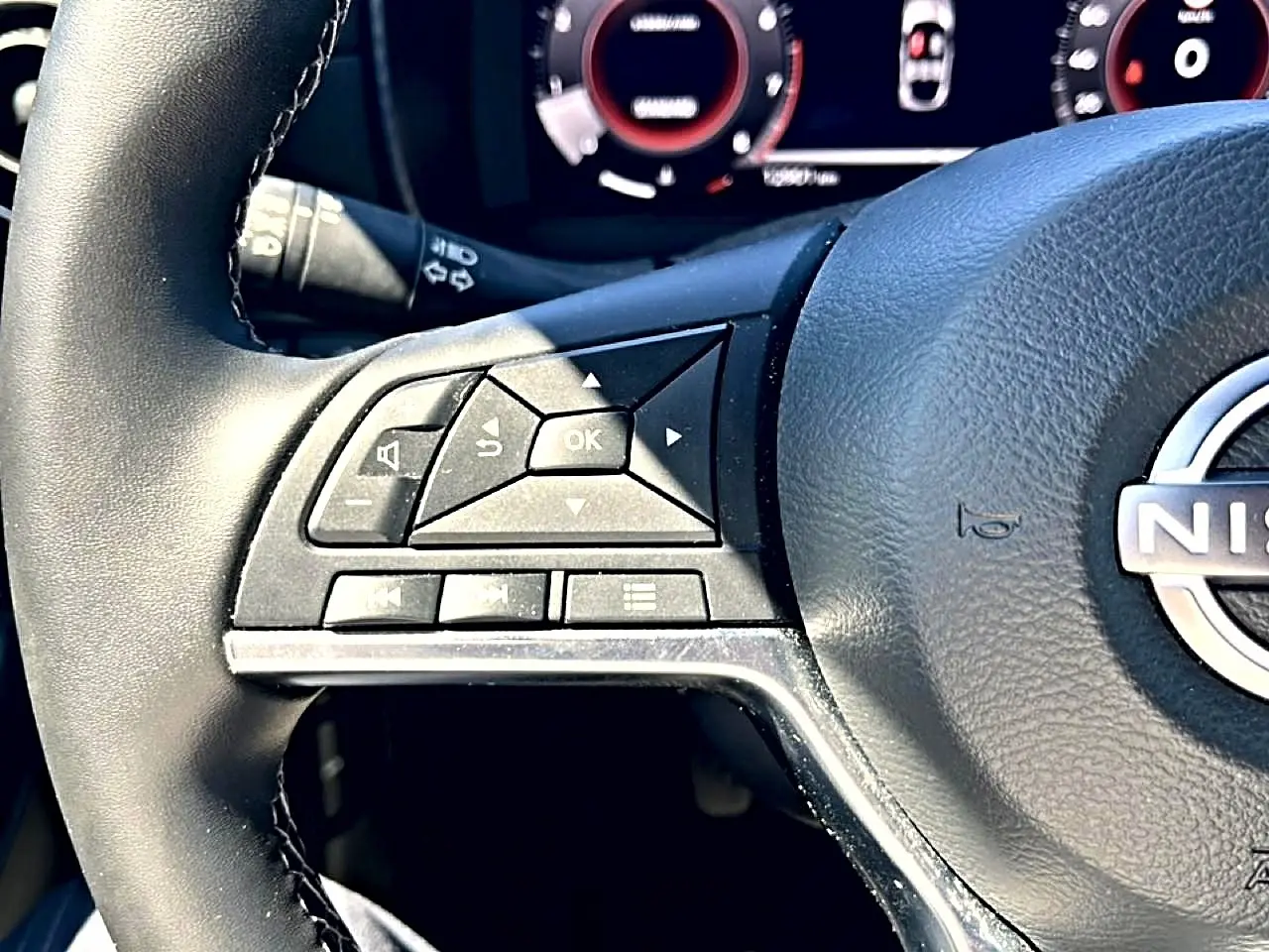 Gros plan sur les commandes multifonctions à gauche du volant cuir noir du Nissan Juke gris 2025, tableau de bord en arrière-plan.