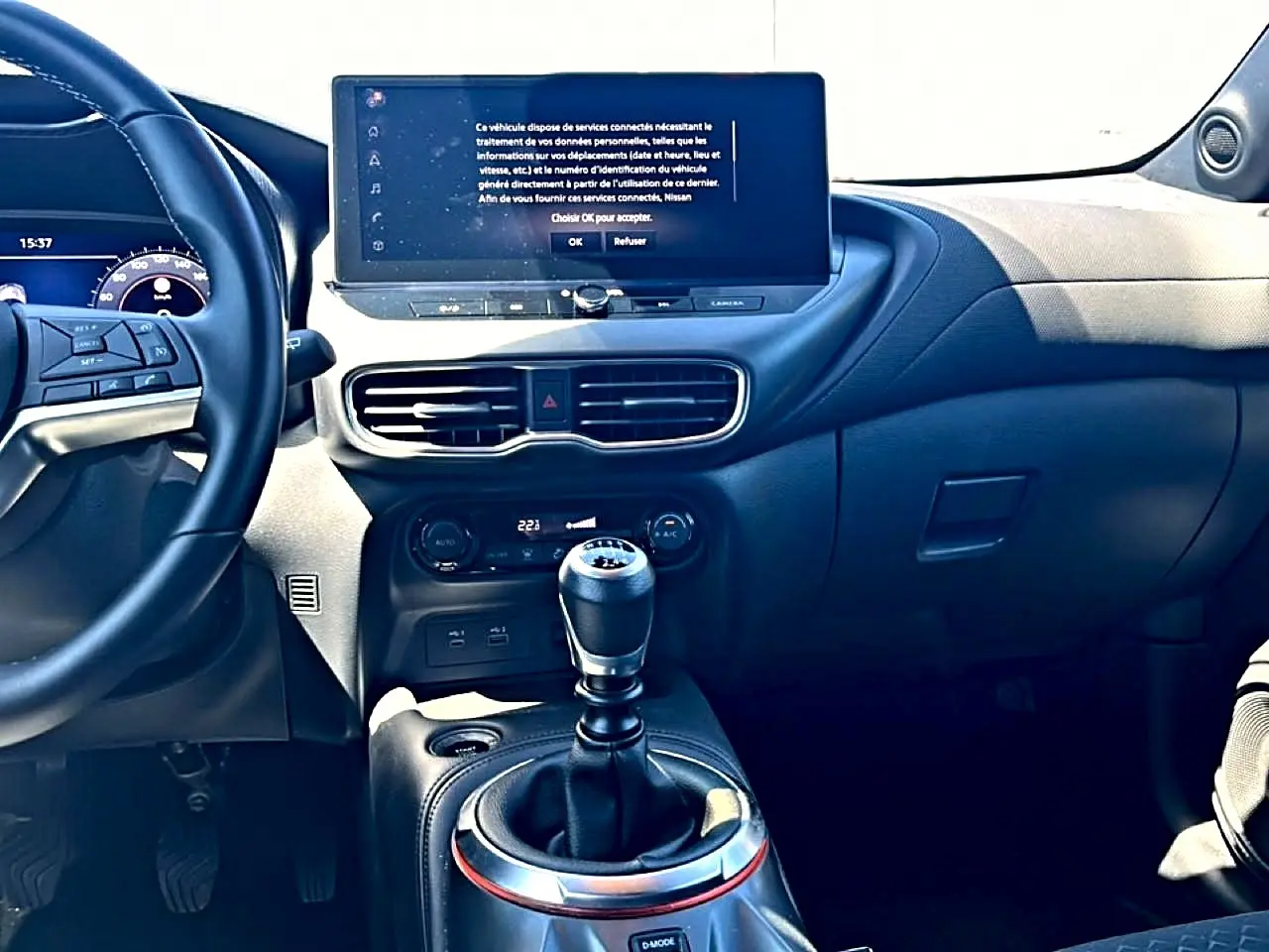 Intérieur du Nissan Juke 2025 vu de face, volant cuir à gauche, écran tactile central et levier de vitesse manuel.