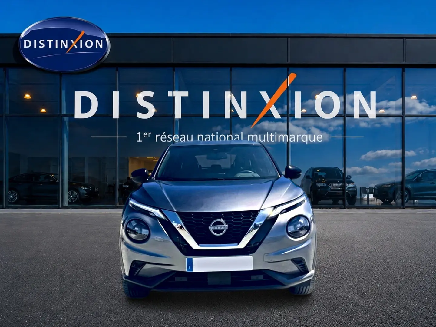 Vue avant d'un Nissan Juke gris 2025 avec calandre en V chromée, phares ronds et logo Nissan visible.