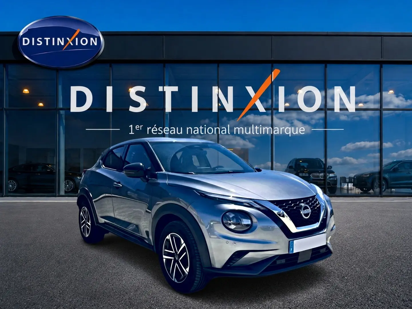 Nissan Juke gris 3/4 avant droit, avec jantes alu et calandre distinctive, devant une vitrine Distinxion.