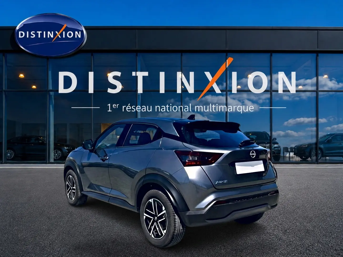 Vue 3/4 arrière droite d'un Nissan Juke gris 2025 avec jantes alu et feux arrière LED, devant une vitrine Distinxion.