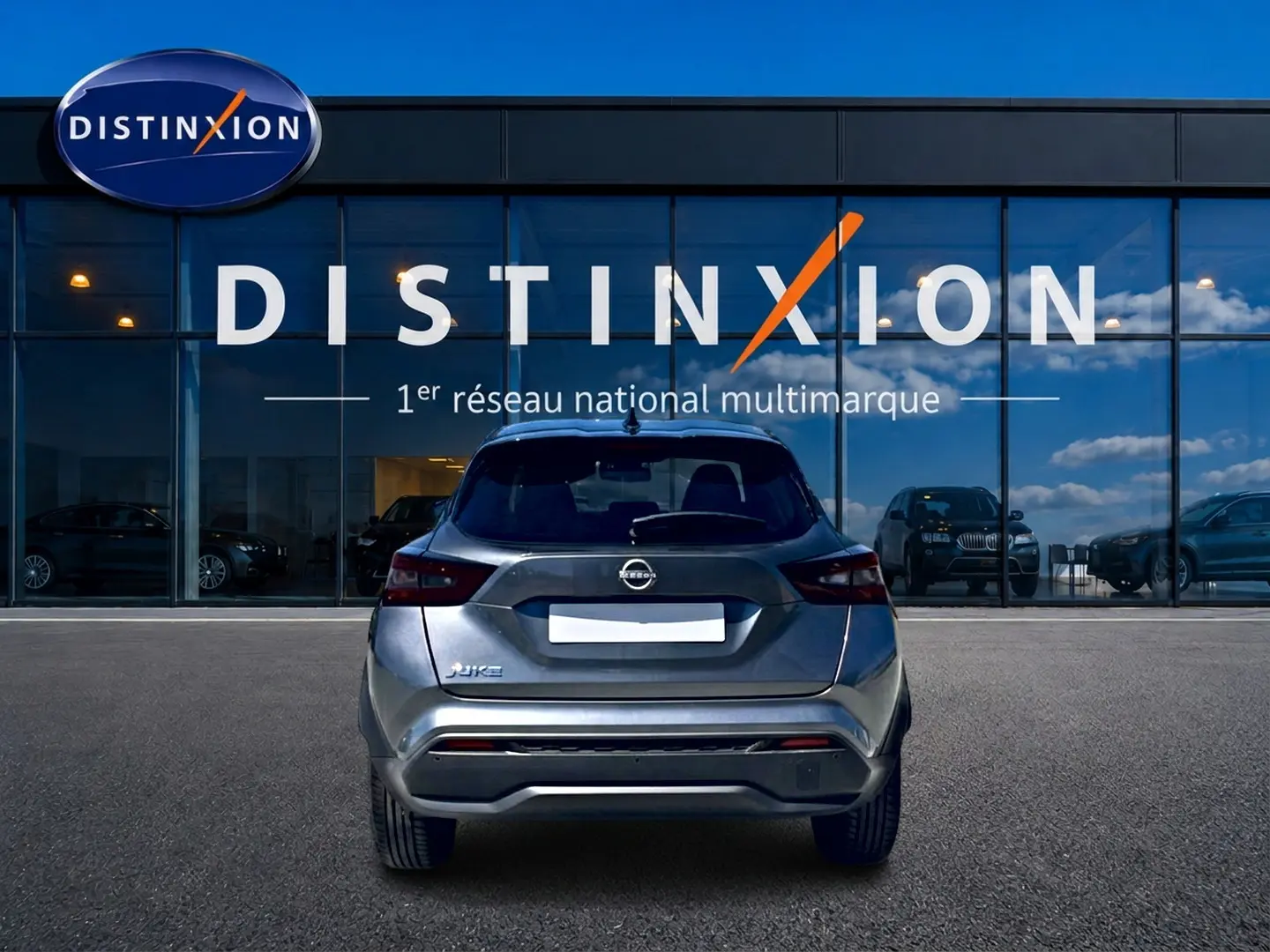 Vue arrière d'un Nissan Juke gris 2025 garé devant une vitrine avec logo Distinxion visible.