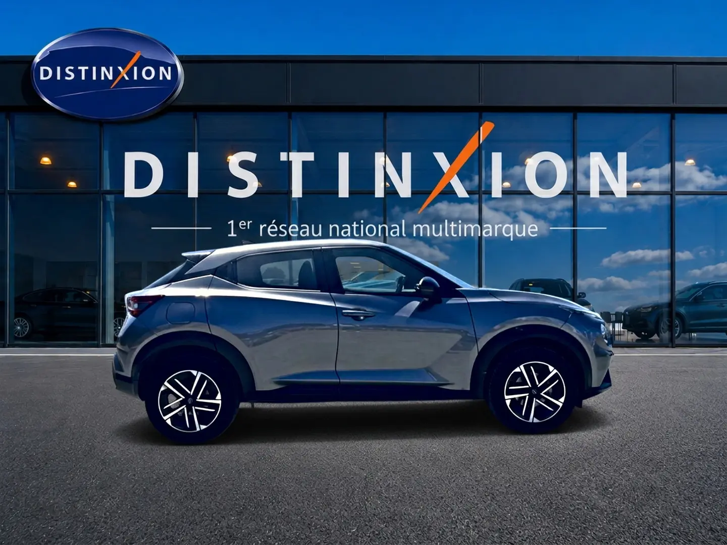 Nissan Juke gris en profil droit devant une vitrine avec logo Distinxion, jantes alliage et lignes dynamiques.