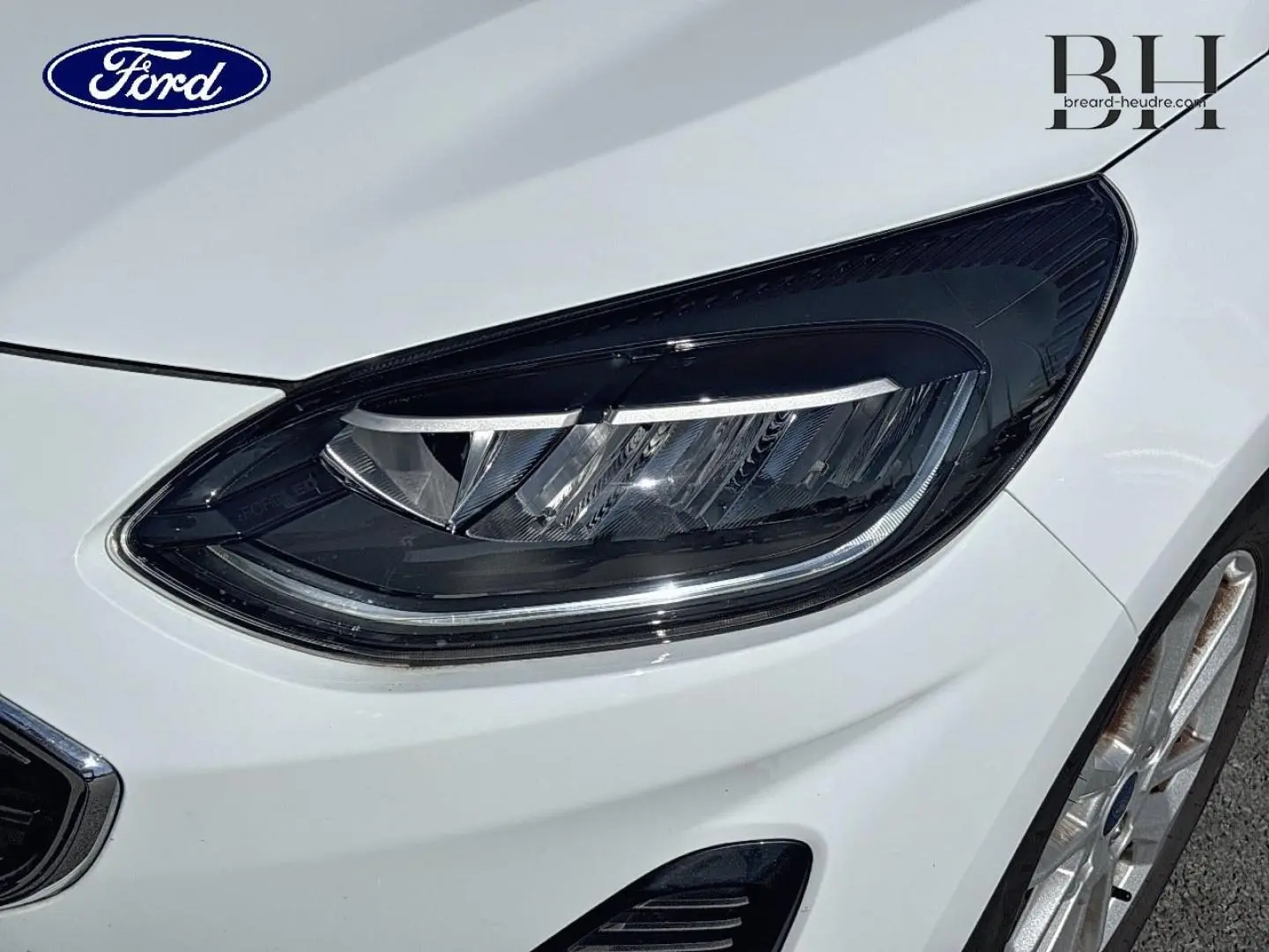 Gros plan sur le phare avant droit et la jante alu d'une Ford Fiesta blanche Glacier 2023, finition Titanium Business.