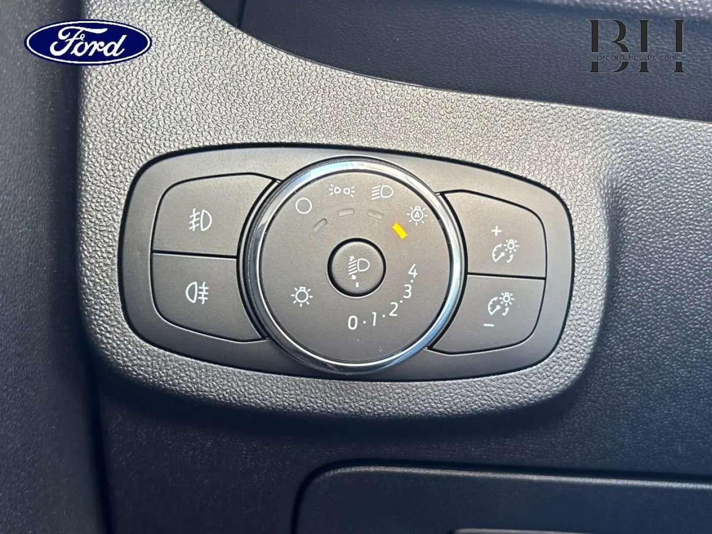 Gros plan sur le bouton de réglage des phares dans l’habitacle noir de la Ford Fiesta Blanc Glacier 2023.