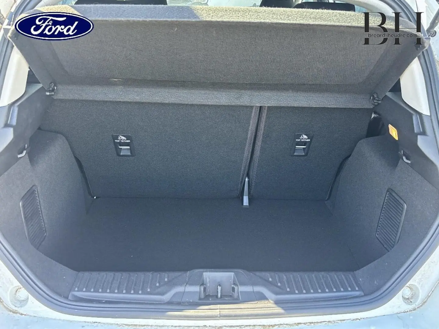 Coffre ouvert vu de l'arrière d'une Ford Fiesta 2023 blanc Glacier, montrant l'espace de rangement vide et la banquette rabattable.