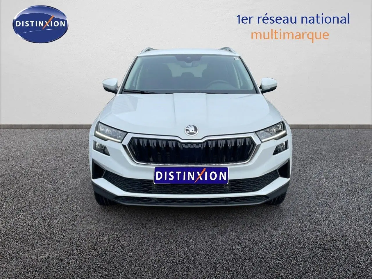 Vue avant d'un Skoda Karoq blanc glacier 2025 avec calandre noire et feux LED, sur fond neutre avec logo Distinxion.