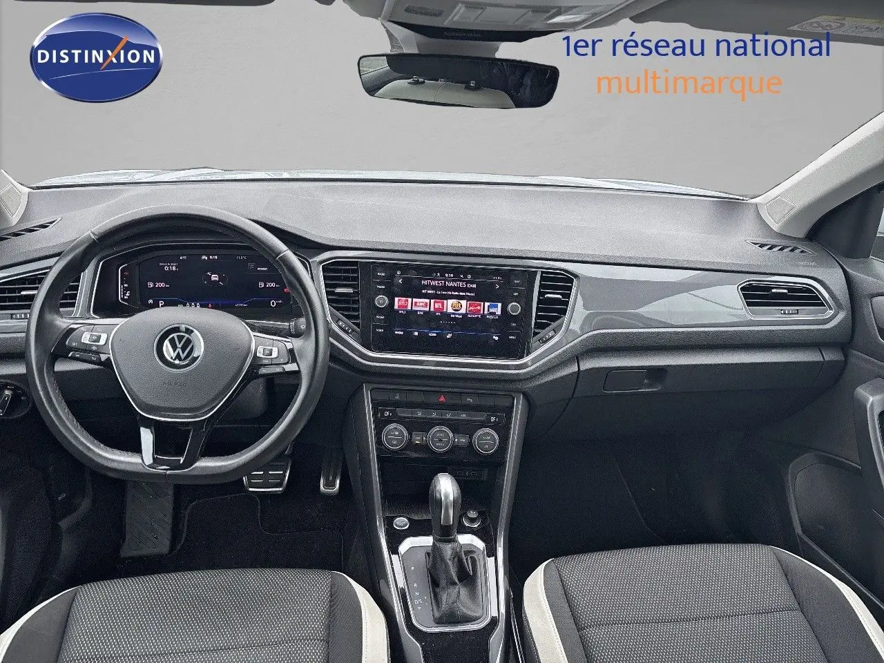 Vue intérieure avant du Volkswagen T-Roc 1.5 TSI 150 CH Carat avec tableau de bord moderne et sièges tissu noir et blanc.