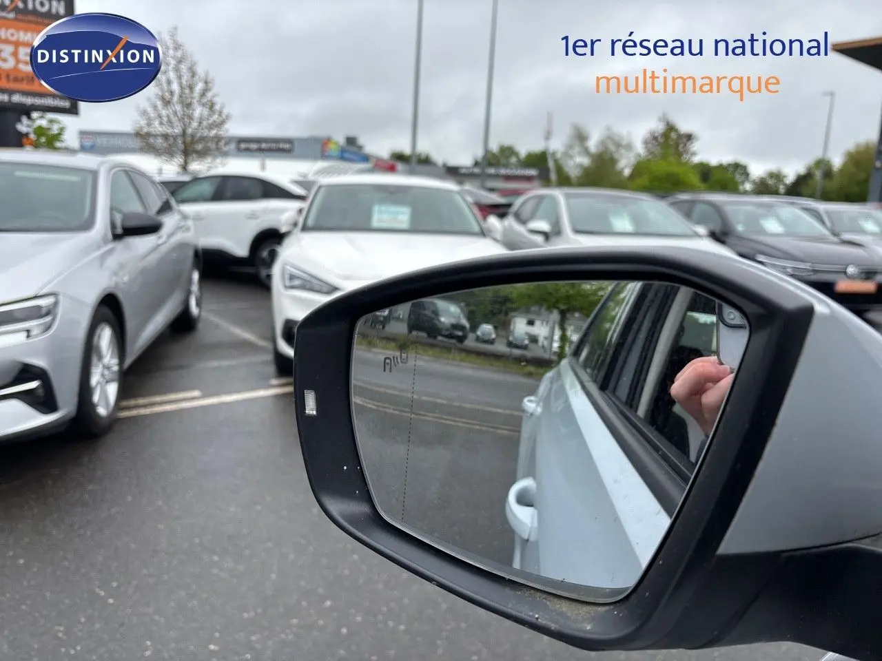 Rétroviseur côté droit d'un Volkswagen T-Roc blanc argent, avec reflet de la portière et main visible.