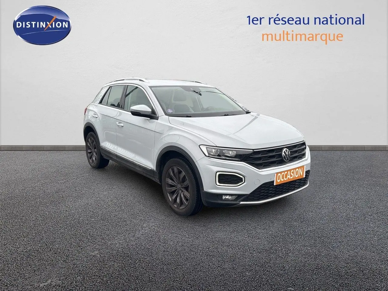 Volkswagen T-Roc blanc argenté en 3/4 avant droit avec jantes foncées sur sol gris.