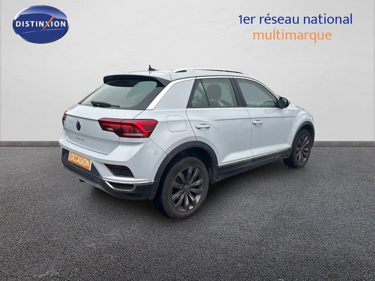 Volkswagen T-Roc blanc argenté vu en 3/4 arrière droit, avec jantes foncées et toit ouvrant visible.
