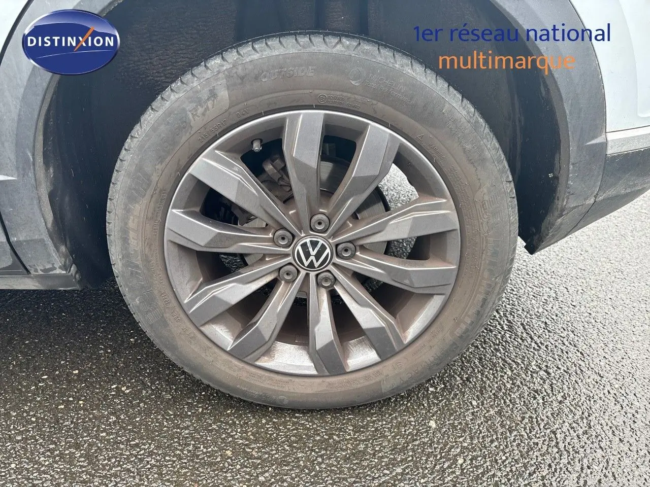 Gros plan sur la roue avant gauche d'un Volkswagen T-Roc blanc argent avec jante alliage grise et logo VW central.