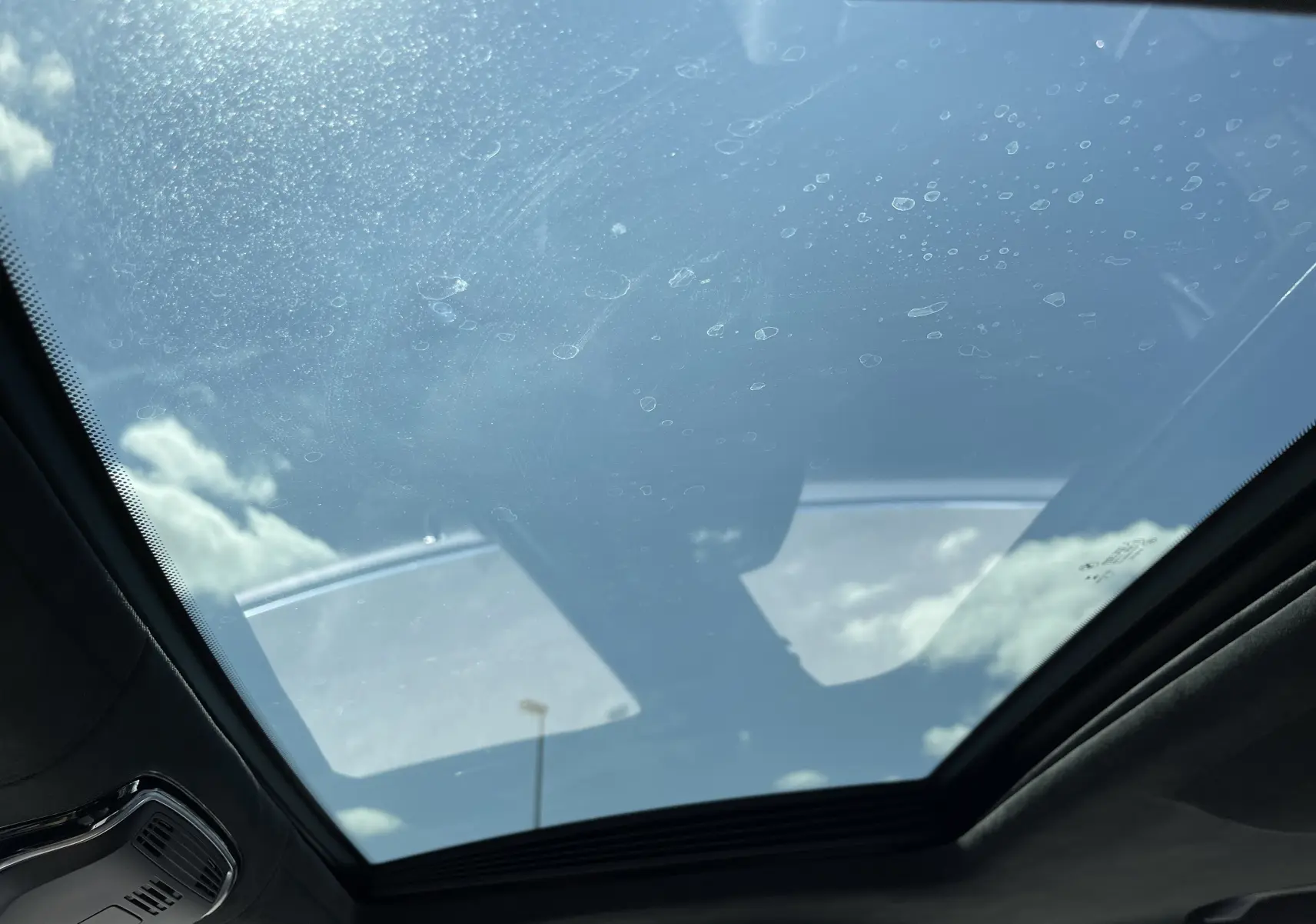 Toit panoramique en verre de la BMW Série 7 G11 noire, vue intérieure vers le ciel nuageux.