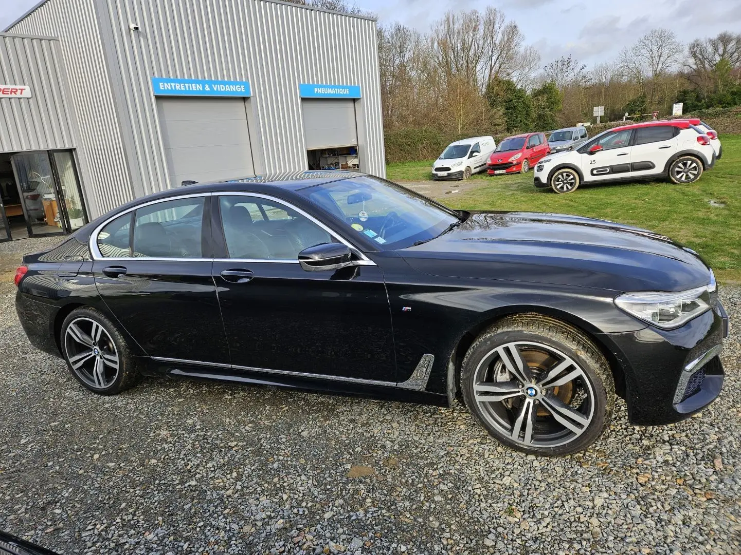 BMW Série 7 G11 noire vue de profil côté gauche, avec jantes sport et détails M Sport visibles.