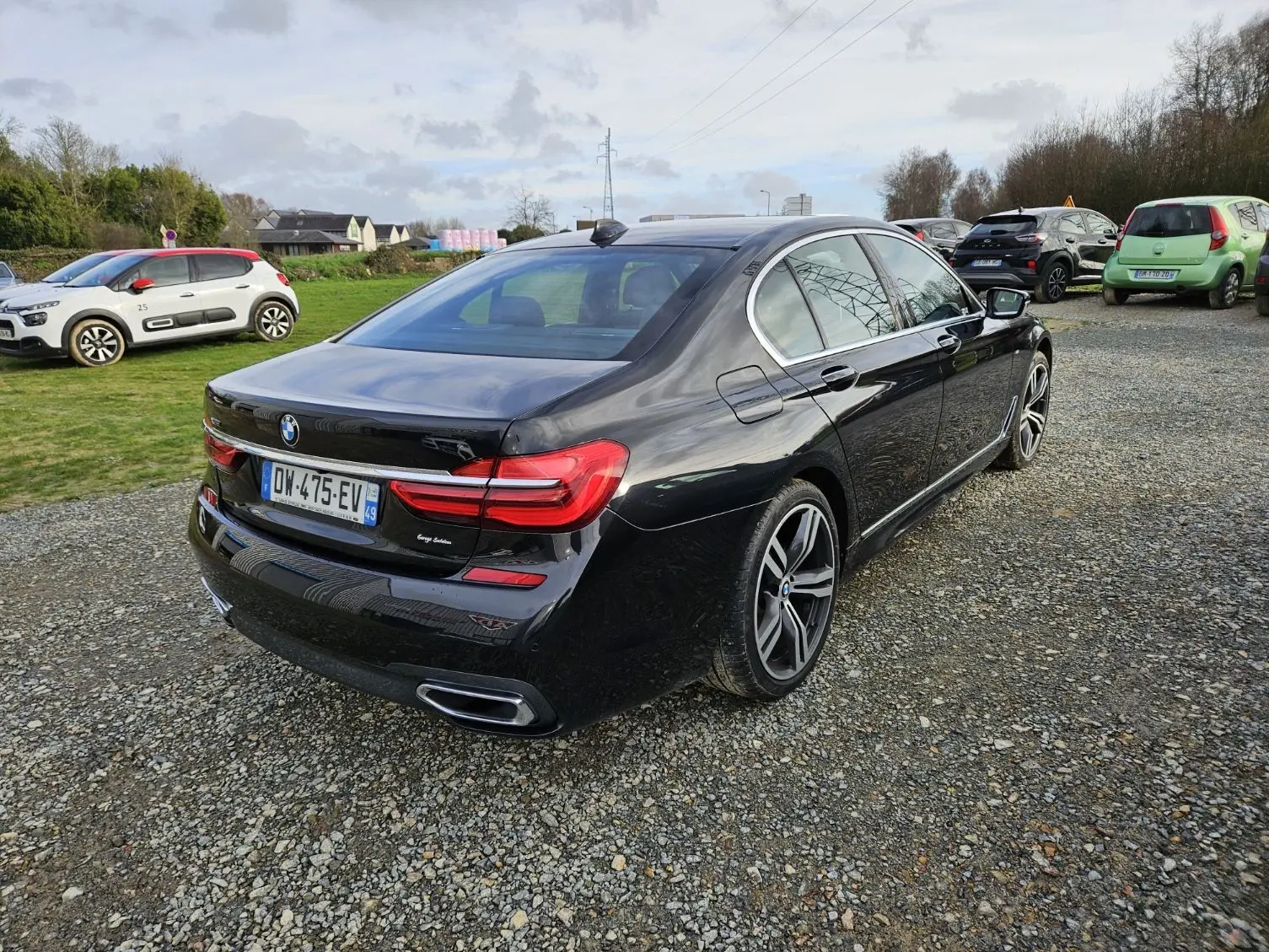 BMW Série 7 G11 noire vue en 3/4 arrière droit sur un parking, avec jantes M Sport et feux LED distinctifs.