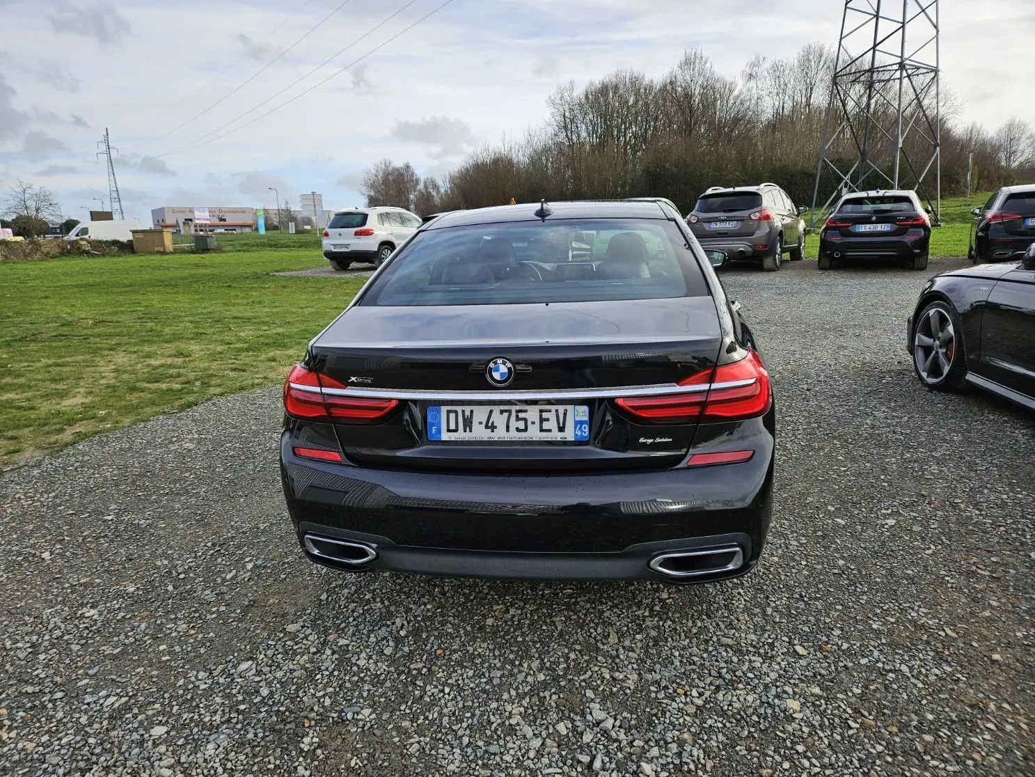 Vue arrière d'une BMW Série 7 G11 noire avec feux LED et double sortie d'échappement dans un parking extérieur.