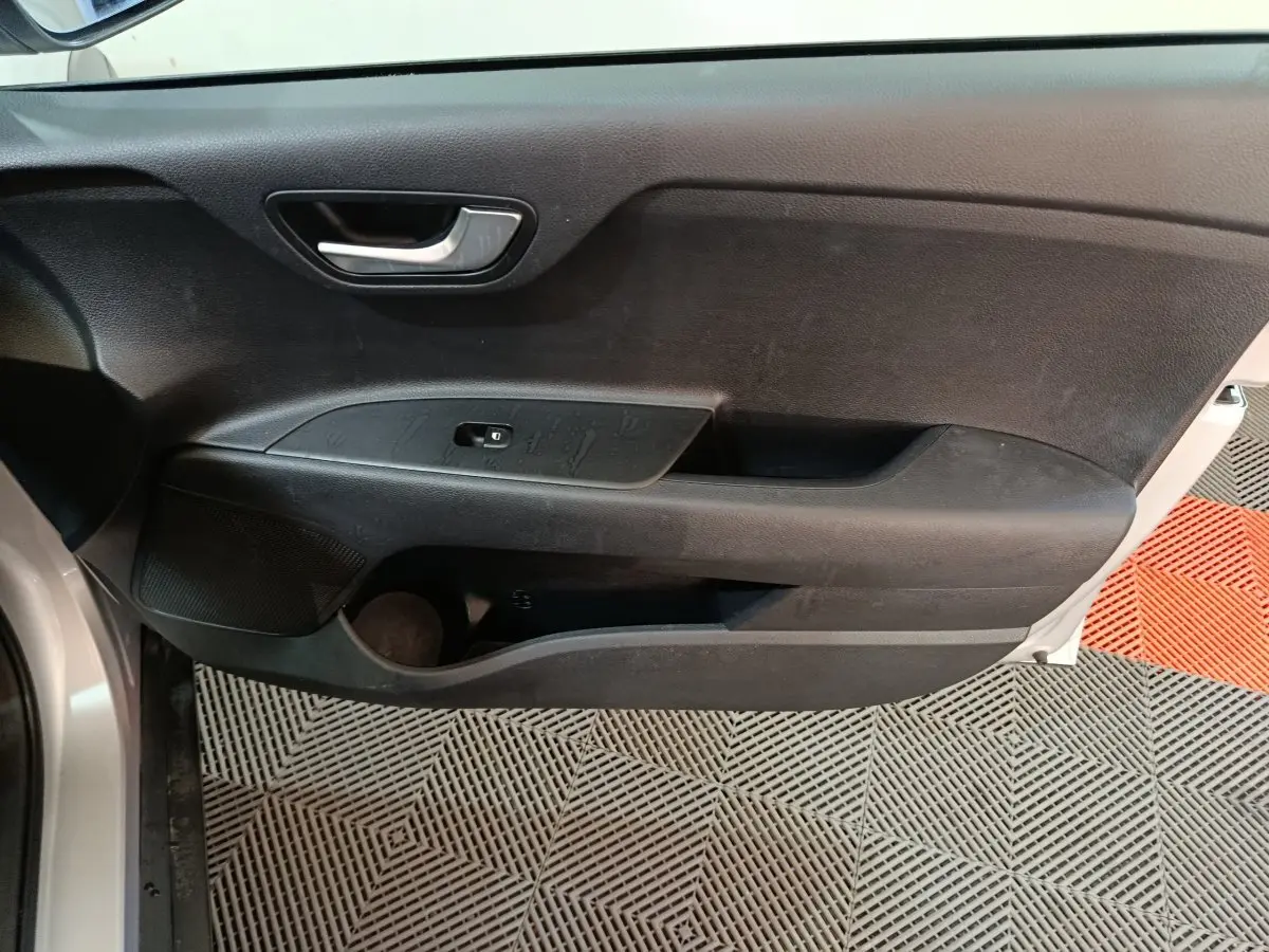 Vue rapprochée de la porte avant gauche noire d’une KIA Stonic gris clair, avec poignée argentée et commande de vitre.