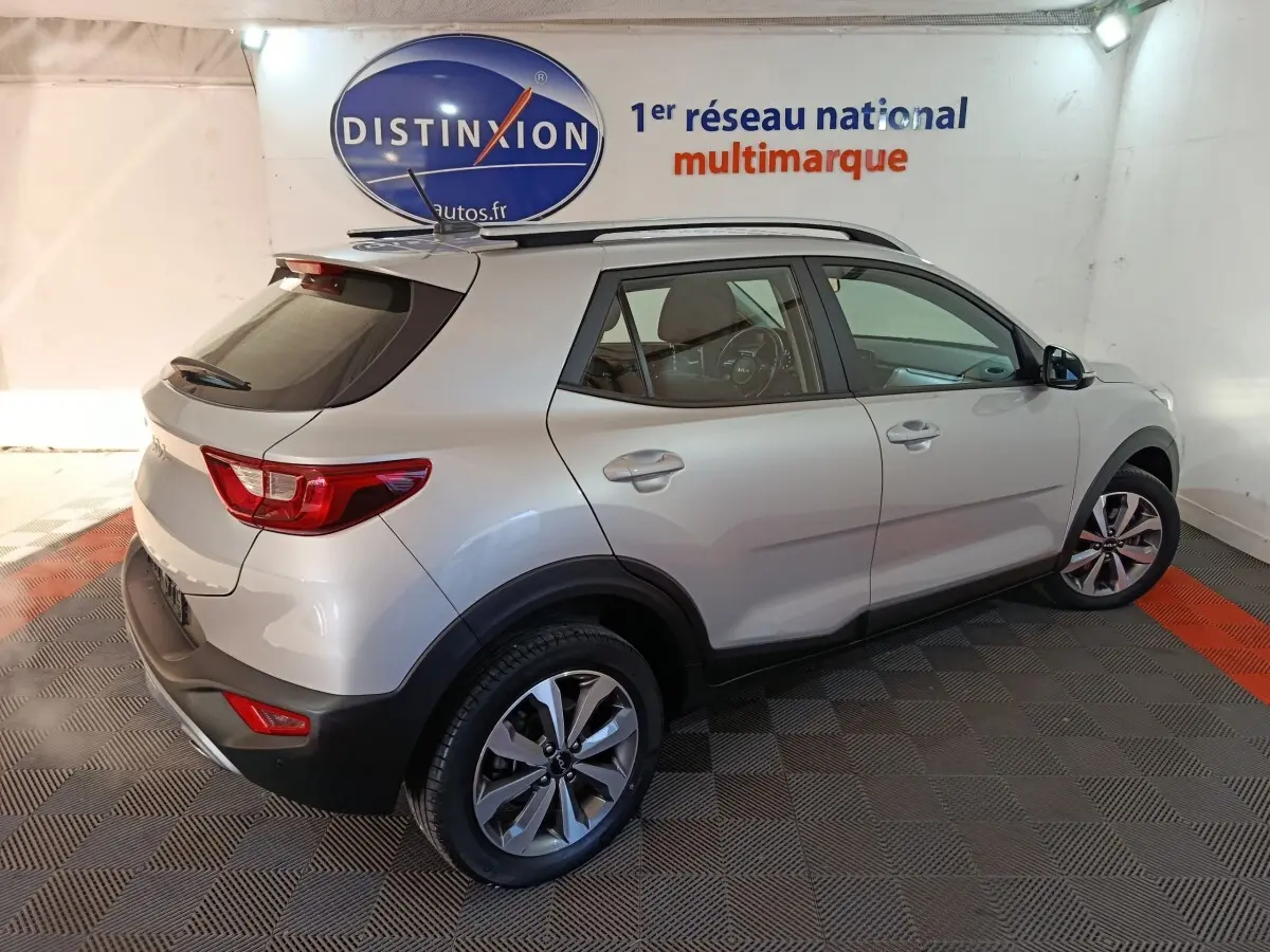 Vue 3/4 arrière droite d'un KIA STONIC gris clair 2022, avec barres de toit et jantes alliage visibles en intérieur showroom.