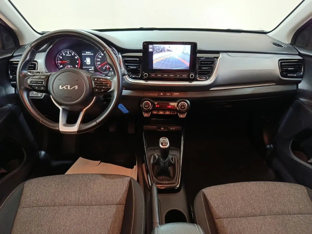 Vue intérieure frontale du tableau de bord gris clair du Kia Stonic 1.0 T-GDI 2022 avec volant multifonction et écran tactile central.