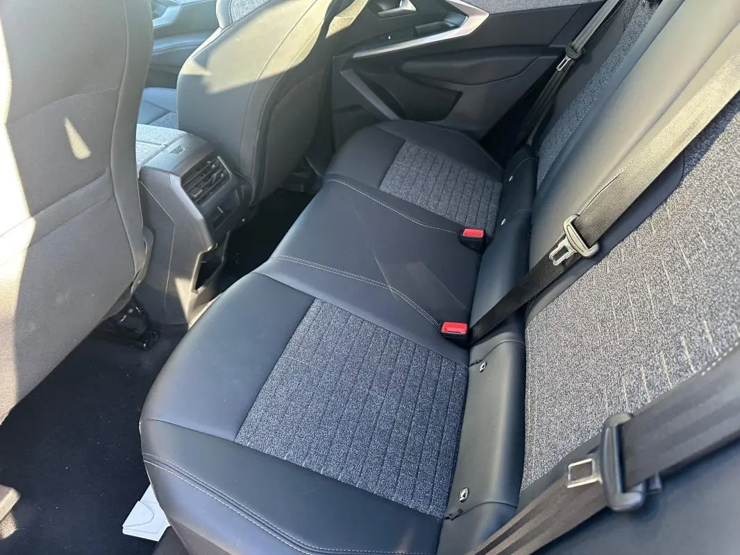 Vue intérieure arrière droite du Peugeot 3008 Hybrid 145 Allure 2025, sièges bicolores tissu et cuir noir.