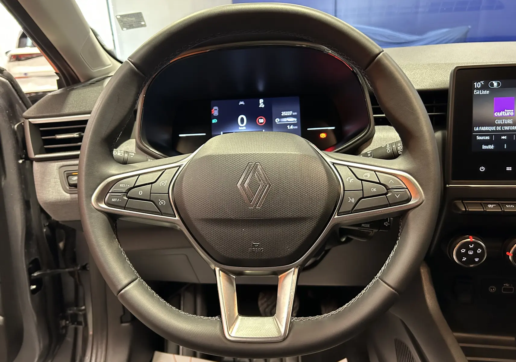 Vue rapprochée du volant cuir noir de la Renault Clio V 2025 avec tableau de bord digital et commandes intégrées.