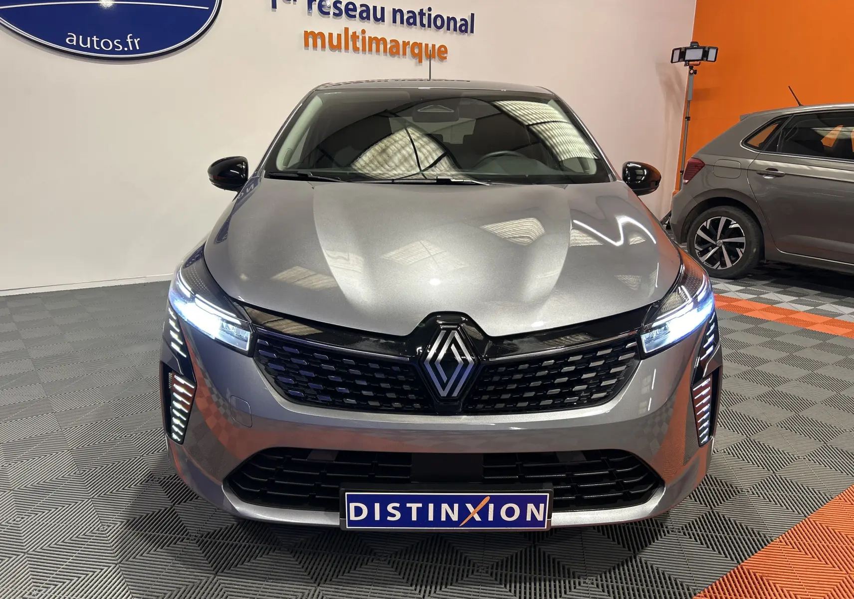 Vue avant d'une Renault Clio V gris schiste métal avec phares LED allumés dans un showroom multimarque.