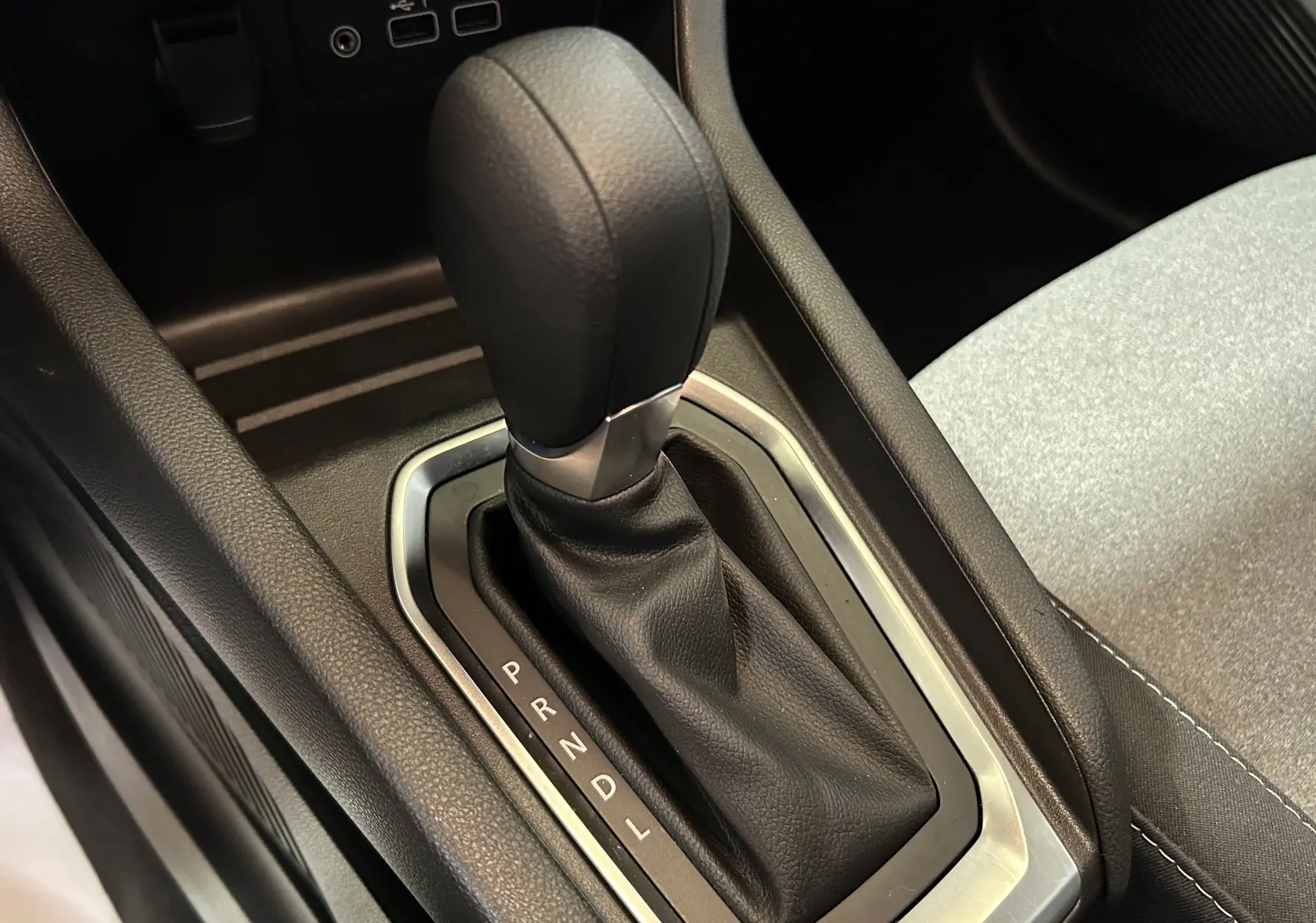 Le levier de vitesse automatique noir de la Renault Clio V TCE 90CH, entouré de garnitures grises et tissu clair adjacent.