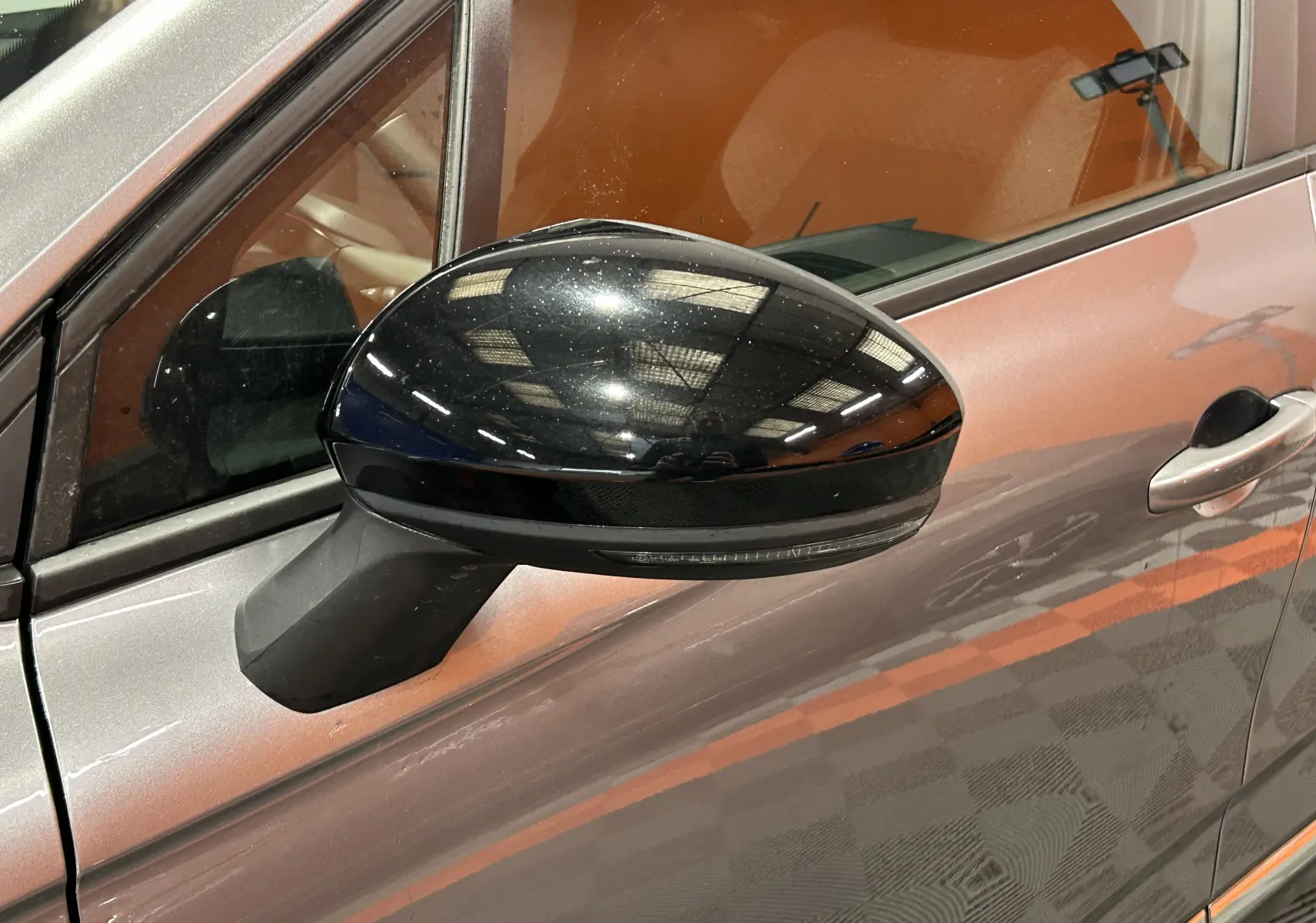 Gros plan sur le rétroviseur noir côté gauche d'une Renault Clio V gris schiste métal, avec reflet intérieur visible.