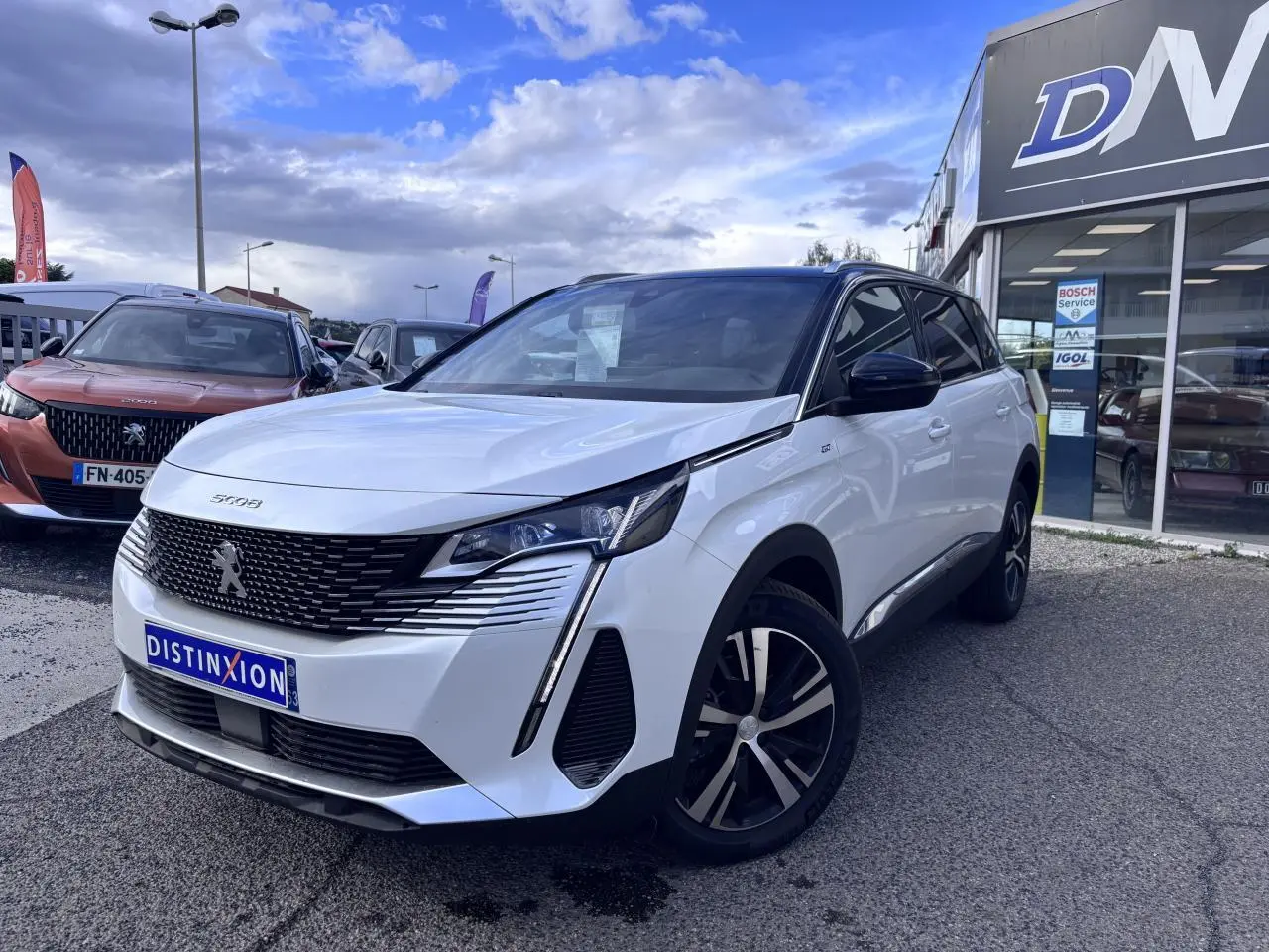 Peugeot 5008 blanc en 3/4 avant droit, avec calandre noire distinctive et jantes alliage bicolores.