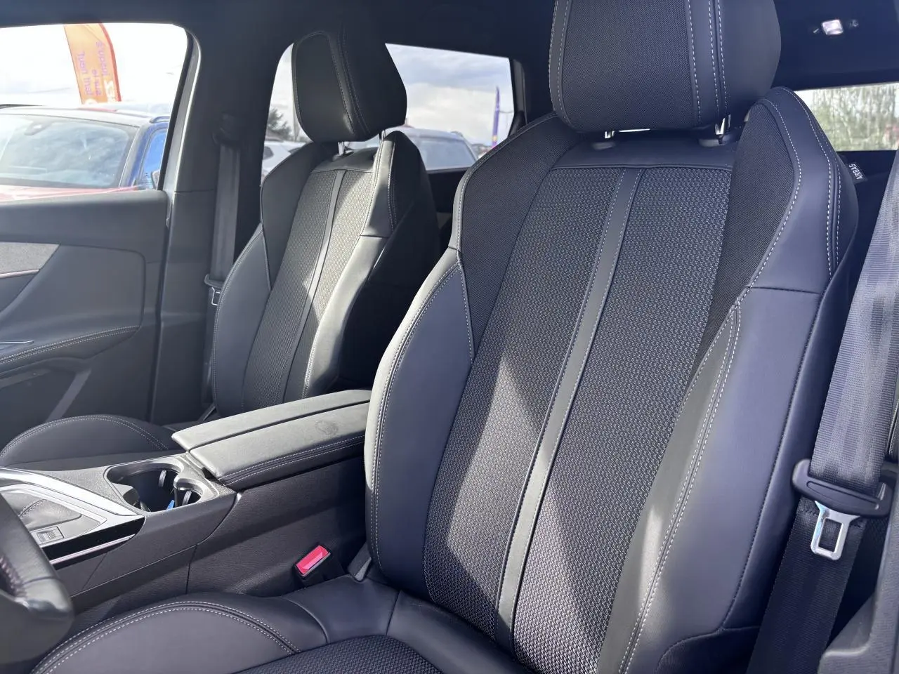 Vue intérieure rapprochée des sièges avant en tissu et cuir noir du Peugeot 5008 GT 2022, avec accoudoir central.