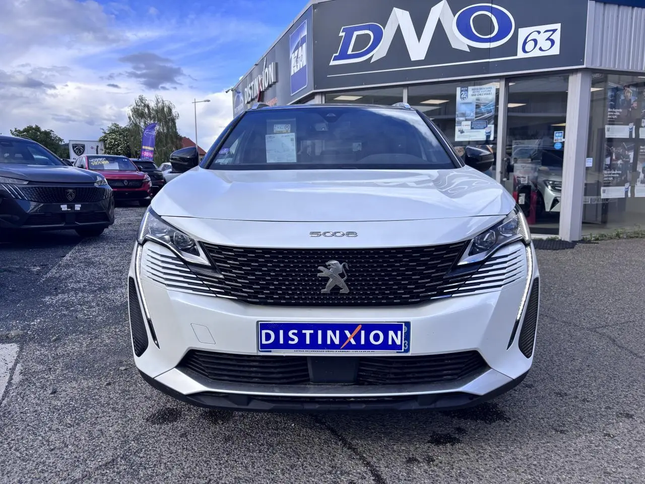 Vue avant d'un Peugeot 5008 blanc 2022 avec calandre noire et phares LED, devant un concessionnaire Distinxion.