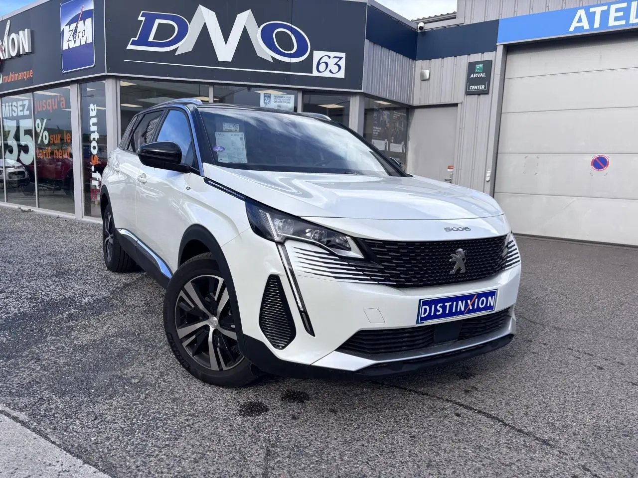 Peugeot 5008 blanc en 3/4 avant droit, avec calandre noire et jantes alliage distinctives, devant un garage.
