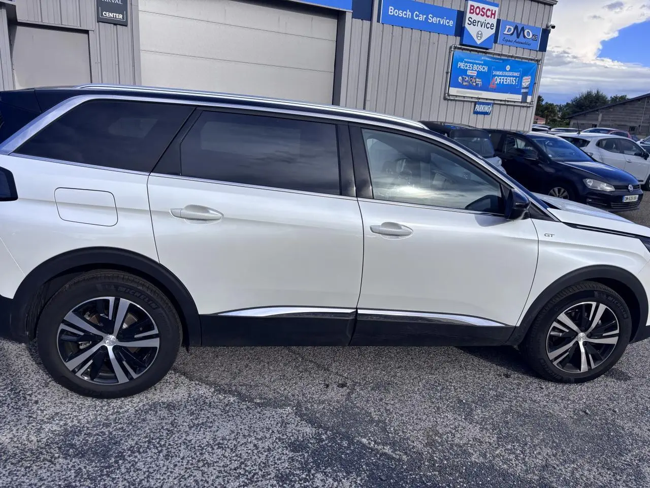 Profil côté droit d'un Peugeot 5008 blanc 2022 GT avec jantes alliage noires et vitres teintées.