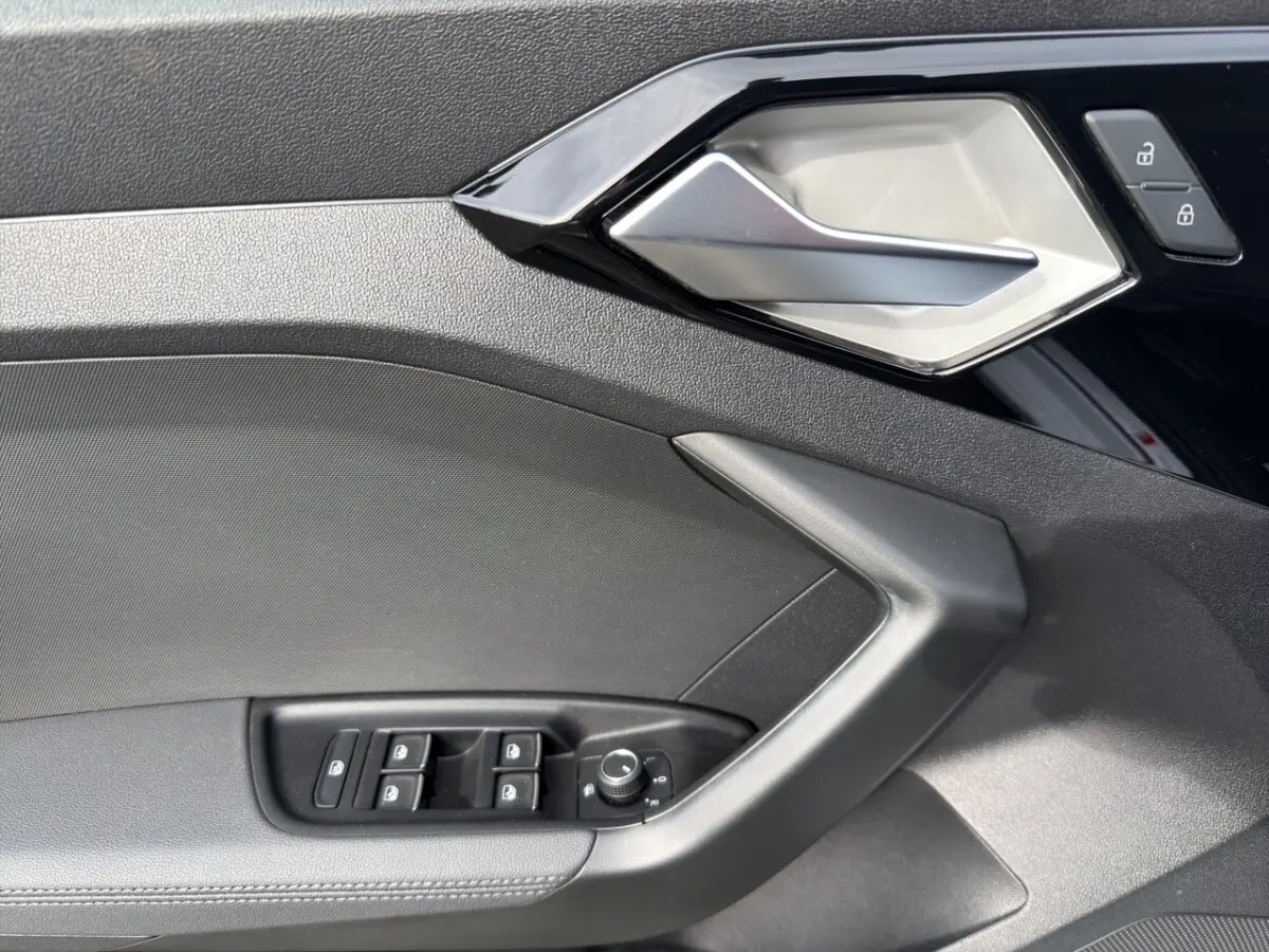Détail de la porte côté conducteur de l'Audi A1 Sportback 2025 blanche, avec commandes des vitres et poignée argentée.