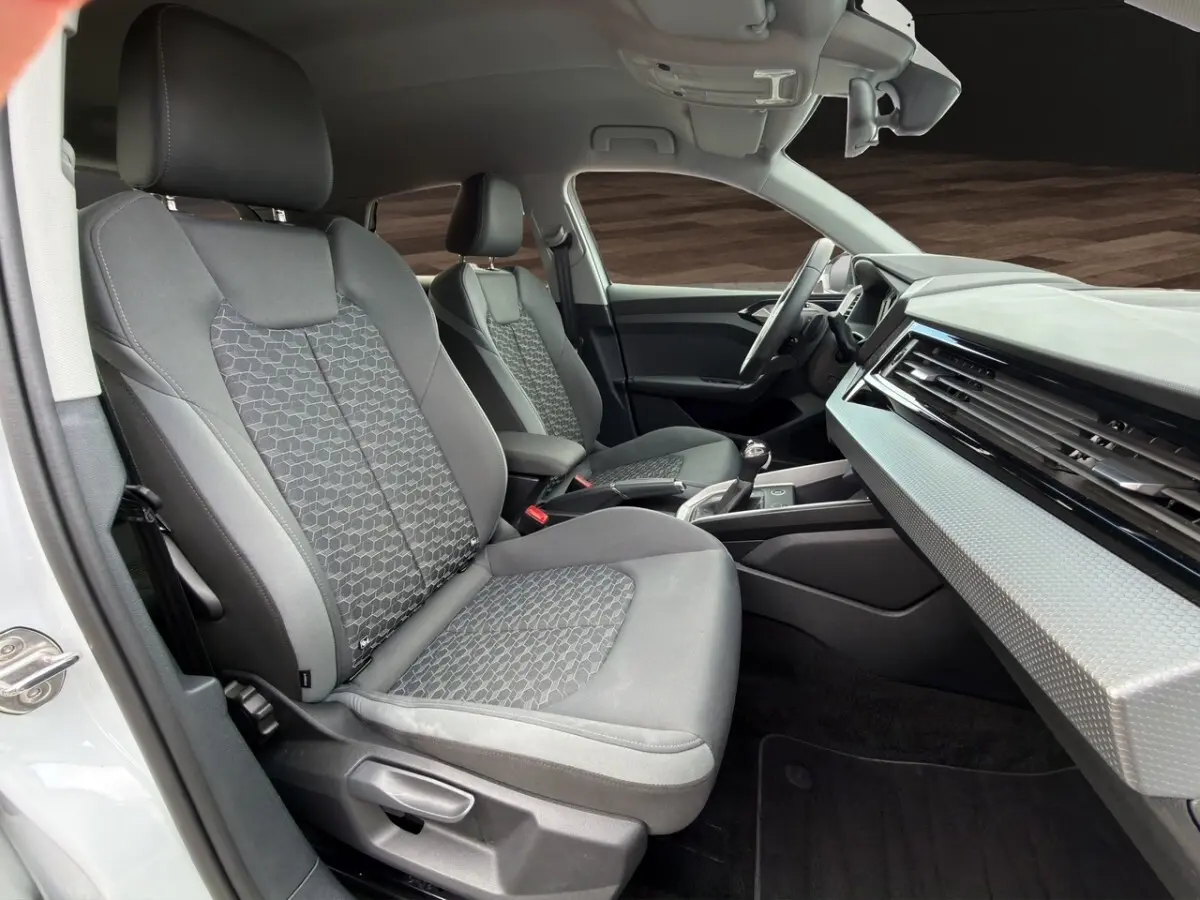 Vue intérieure côté conducteur de l'Audi A1 Sportback 2025 avec sièges gris et tableau de bord moderne blanc texturé.