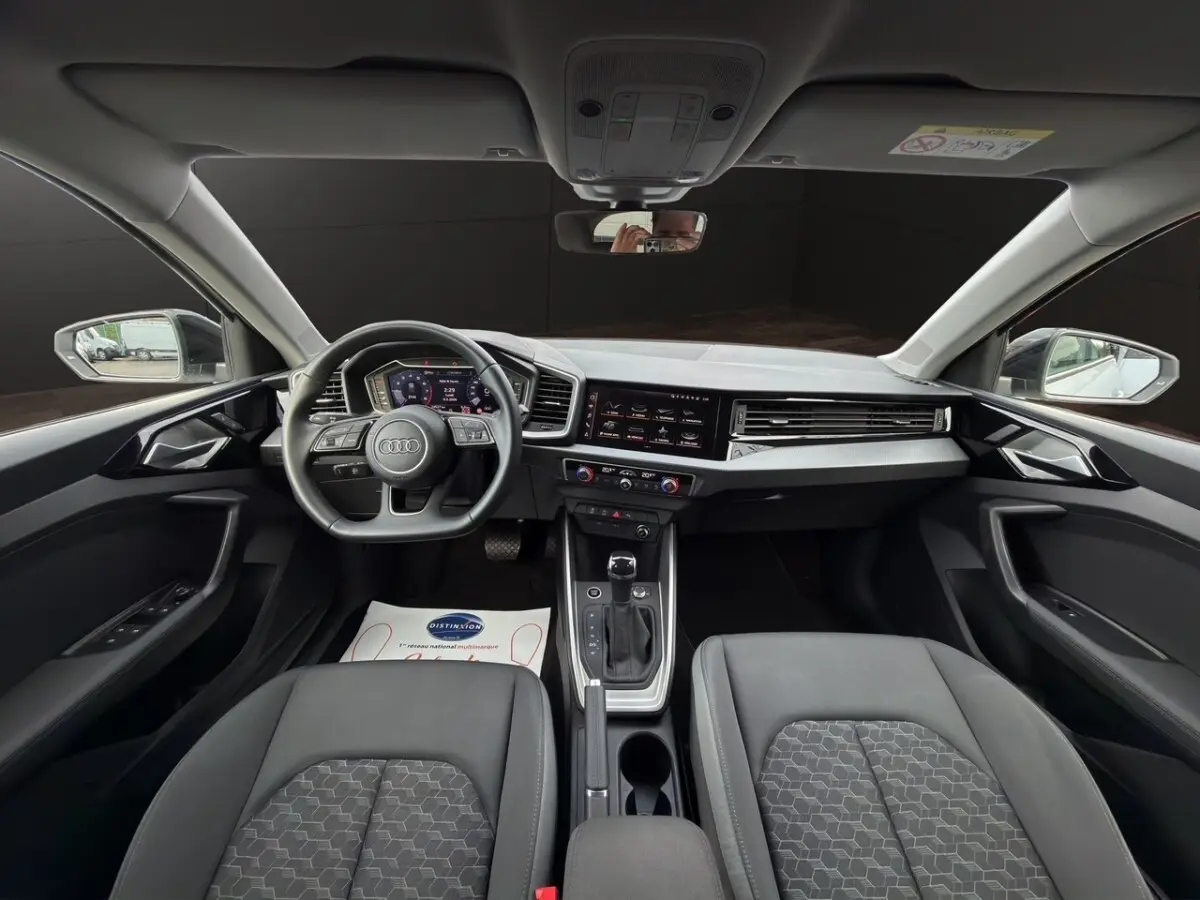 Vue intérieure avant de l'Audi A1 Sportback 2025 avec tableau de bord numérique et sièges gris foncé.