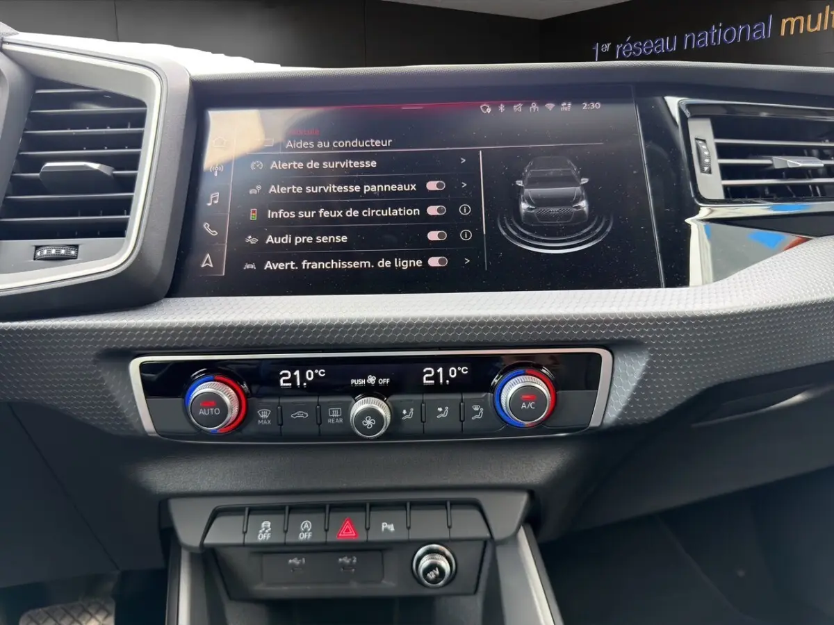Vue rapprochée du tableau de bord de l'Audi A1 Sportback 2025 blanc, avec écran tactile et commandes climatisation digitales.