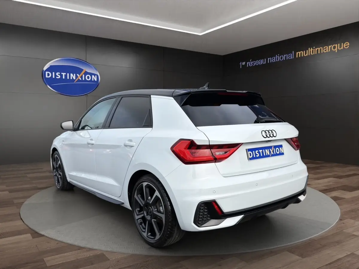 Audi A1 Sportback blanc vue 3/4 arrière droit en intérieur avec toit noir et jantes noires distinctives.