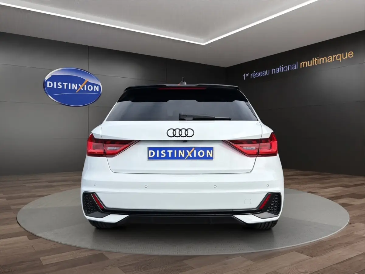 Vue arrière d'une Audi A1 Sportback blanche 2025 avec feux LED et caméra de recul en showroom.