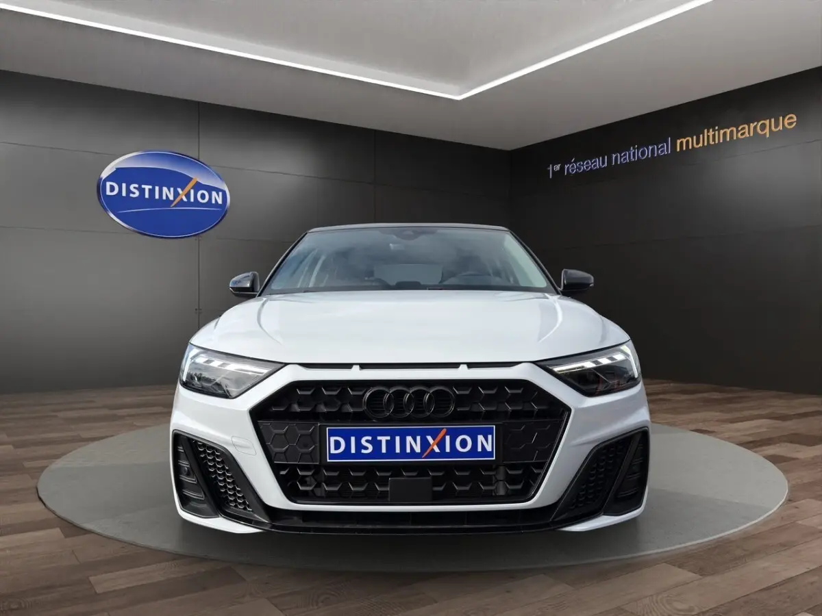 Vue frontale d'une Audi A1 Sportback blanche 2025 avec calandre noire et phares LED, en showroom Distinxion.
