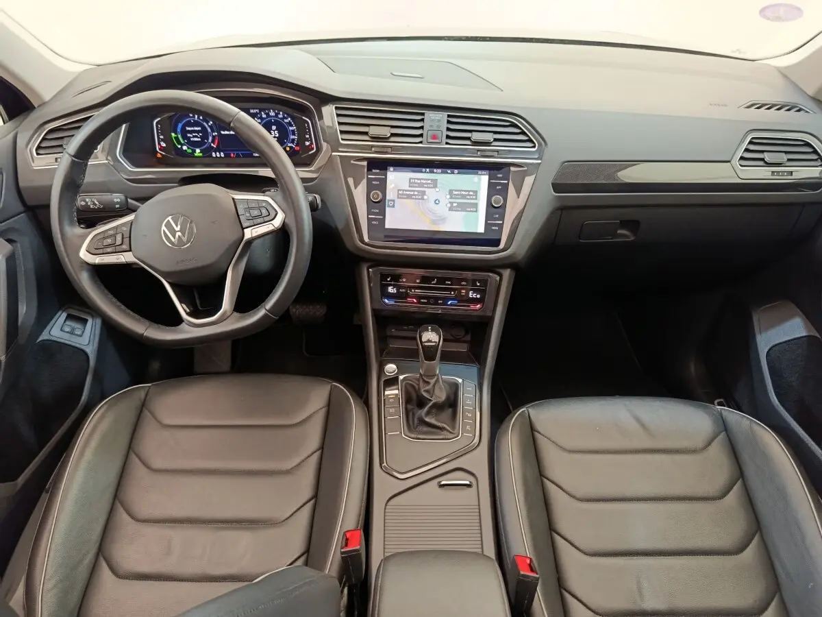 Vue intérieure avant du Volkswagen Tiguan 1.4 eHybrid 2022 avec tableau de bord numérique et sièges en cuir noir.